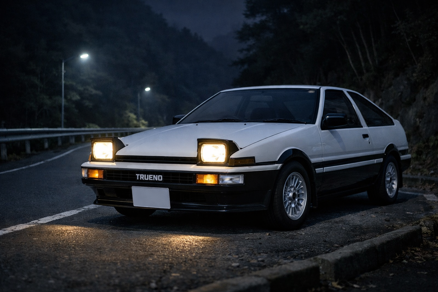 夜の日本の峠に停まる白黒ツートンのトヨタAE86。ヘッドライトの光が細い路面を静かに照らしている。