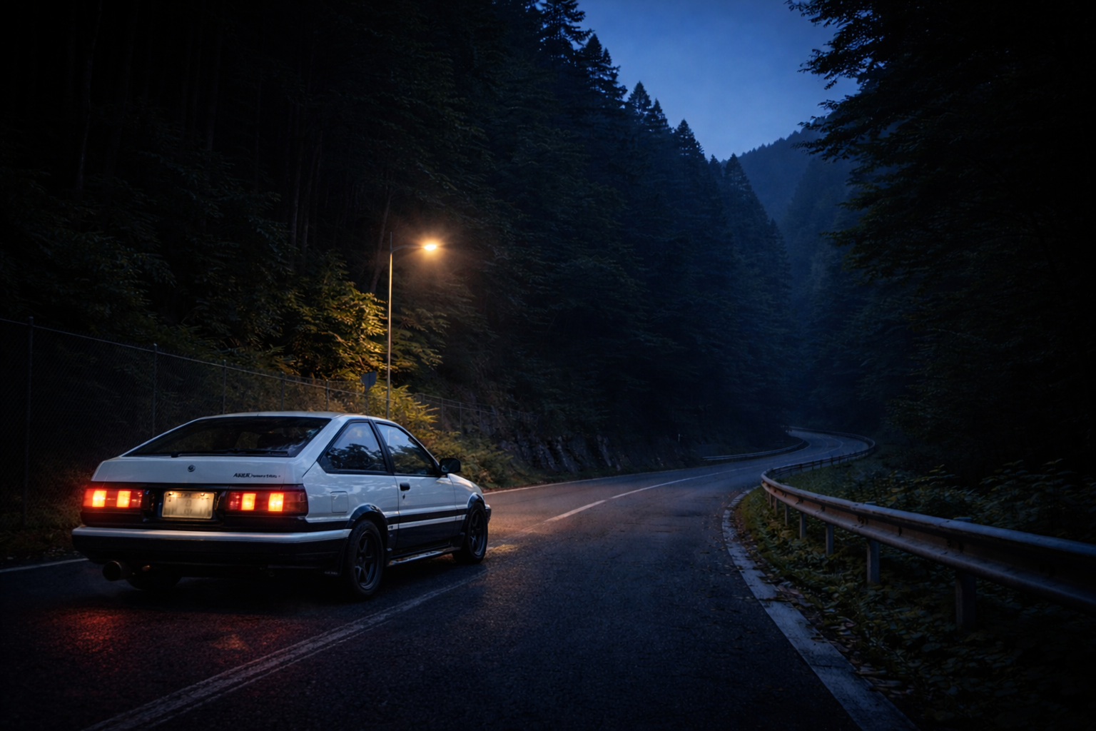 An AE86 stopped at the entrance of a quiet mountain pass before dawn, illuminated by a single streetlight and surrounded by forest.